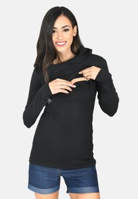 Maglietta nera a maniche lunghe con cappuccio e dettaglio di apertura frontale. Realizzata in materiale morbido, dal design aderente, abbinata a pantaloni denim shorts.