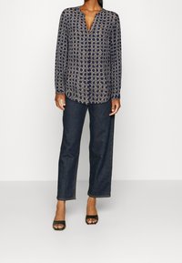 Mörkblå blus med lång ärm, cirkulärt mönster och V-ringning. Matchas med mörka jeansbyxor med vida ben och svarta öppna klackar.