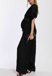 Schwarzes plissiertes Maxikleid mit kurzen Puffärmeln und einem olivgrünen gemusterten Taillengurt, kombiniert mit einer schwarzen Clutch und schwarzen High-Heels.