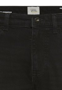 Zwarte spijkerbroek met knoopsluiting, riemlussen en Camel Active merklabel aan de binnenkant van de tailleband.