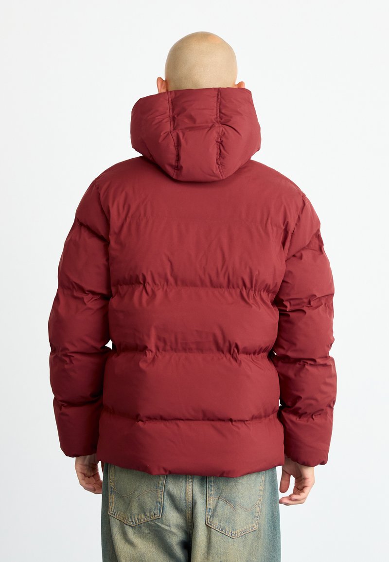 Giacca puffer bordeaux con cappuccio, caratterizzata da un design imbottito e polsini elastici. La vista posteriore mostra un materiale liscio e una texture morbida.