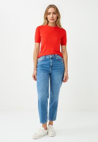 Rode kortom mouw gebreide top gecombineerd met lichtblauwe high-waisted jeans en witte sneakers. Heeft een eenvoudig, aansluitend ontwerp.