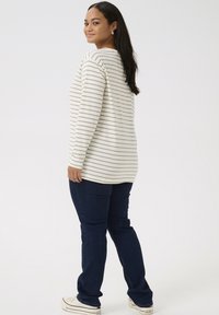 Long-sleeve, cream top with light gray stripes paired with dark blue jeans. Model faces slightly back, wearing white sneakers. Smooth texture.