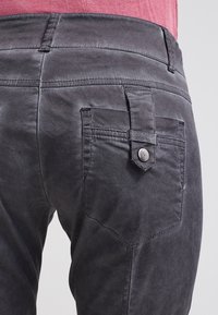 Donkergrijze broek met een gladde textuur, voorzien van een onderscheidend ontwerp voor de achterzak en metalen knoophardware. Smal gesneden pasvorm met riemlussen.