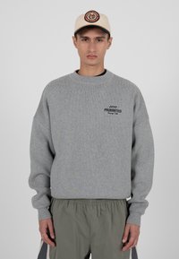 Szara oversizeowa bluza z prążkowymi mankietami i kołnierzem, ozdobiona wyhaftowanym napisem "ZABRONIONE". Połączona z luźnymi oliwkowymi spodniami.