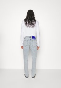 Ljust tvättade denimjeans, rak passform, med bakfickor med blå etikett, i kombination med en vit långärmad skjorta.