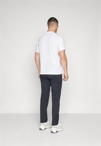 Witte korteflens t-shirt gedragen met donkergrijze broek. De broek heeft een slim fit, en de outfit wordt compleet gemaakt met witte sneakers.