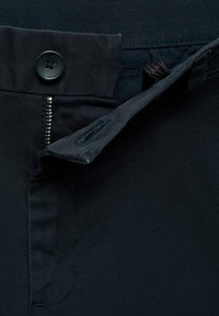 Schwarze Hose mit Reißverschluss, Knopfverschluss und strukturiertem Bund. Das Material wirkt glatt mit einem dezenten Glanz.