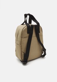 Kahvakuprik, mis on valmistatud kangast, mustade rihmadega, ümar kuju, küljetaskud ja kangatekstuur. Omab reguleeritavaid rihmasid ja õmblusdetailsusi.