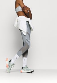 Outfit sportivo composto da un reggiseno sportivo grigio chiaro, leggings grigi con blocchi di colore e sneakers verde menta con dettagli corallo, abbinate a calzini bianchi.