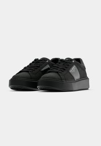 Melnas sporta kurpes ar gludu ādas augšdaļu, mežģīņu priekšpusi un plakanu gumijas zoli. Sānos ir spīdīga paneļa ar zīmolu. Klasisks zema augstuma dizains.