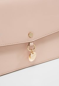 Borsa a tracolla in pelle rosa con una finitura liscia, chiusura a patta, accessori in oro e un ciondolo rotondo attaccato tramite un anello metallico.