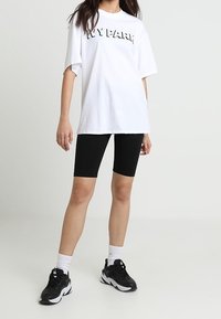 Camiseta blanca de gran tamaño con letras negras "IVY PARK", combinada con pantalones cortos de bicicleta negros y zapatillas deportivas en blanco y negro.