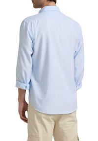 Camisa abotonada de un azul claro con mangas enrolladas, detalle en el yugo trasero, tejido suave y dobladillo recto, combinada con pantalones beige claros.