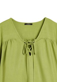 Zielona lniana bluzka z dekoltem w kształcie litery V, z detalem w postaci wiązania, marszczonym materiałem pod dekoltem oraz lekką teksturą.