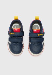 Baskets pour enfants bleues avec des bandes velcro, accents rouges et un logo Superman. Semelle texturée et design respirant.