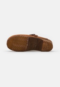 Suola di un sandalino in pelle marrone con grip in gomma testurizzata e tacco in legno, evidenti segni della misura sul legno.