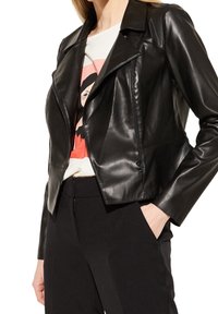 La veste de moto en cuir noir présente un design ajusté, des revers angulaires et une poche zippée à l'avant, associée à un tee-shirt graphique décontracté.