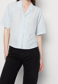 Light blue short-sleeve shirt with a subtle floral pattern, button-down front, and a relaxed fit. Smooth fabric and notched collar design.