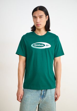 Green cotton t-shirt with a round neck, featuring a large white Reebok logo on the front. The fit is relaxed, complemented by blue denim jeans.