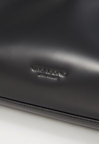 Borsa a mano in pelle nera con una texture liscia. Presenta il marchio in rilievo "VAGABOND". Design minimalista con linee pulite e senza ulteriori motivi.