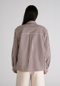 Langærmet skjorte i bordeaux og creme farvet med lodrette striber. Har en krave og knapmanchetter. Stoffet har et blødt, tekstureret udseende.