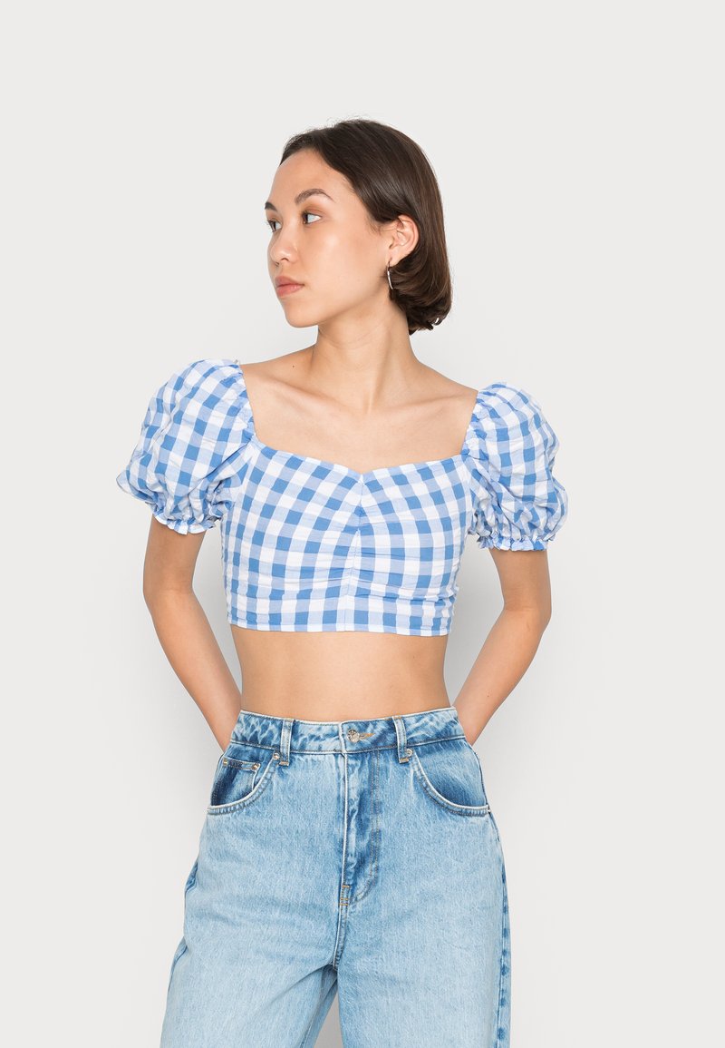 Top cropped em padrão xadrez azul e branco com mangas bufantes, decote quadrado e detalhes franzidos, combinado com calças jeans altas de cintura clara.