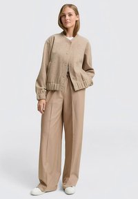 Bež pleteni kardigan s okruglim izrezom, gumbima sprijeda i rebrastim manžetama, uparen sa širokim bež hlačama i bijelim tenisicama.