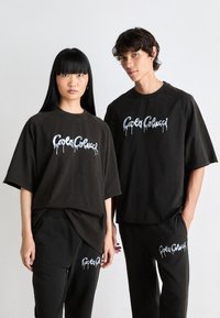 Zwarte oversized t-shirts en bijpassende sweatpants met witte, druppelende tekstgraphics. De stof lijkt zacht met een relaxte pasvorm en minimale naden.