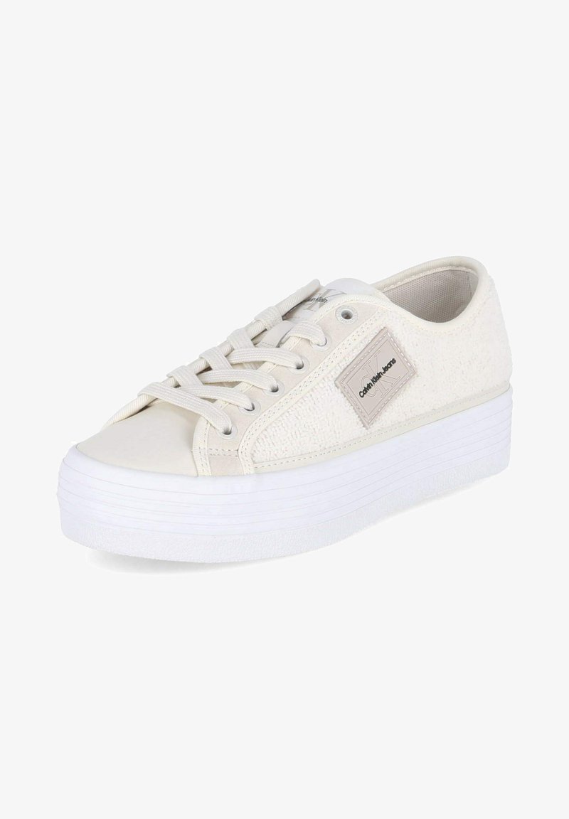 Baskets plates blanches avec une tige en tissu texturé, un embout lisse et des lacets plats. Présente un patch logo sur le côté et une semelle en caoutchouc.