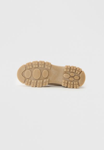 Suola di scarpa in gomma di colore beige con superficie testurizzata, caratterizzata da ampronte circolari e rettangolari di grandi dimensioni per maggiore aderenza e stabilità.