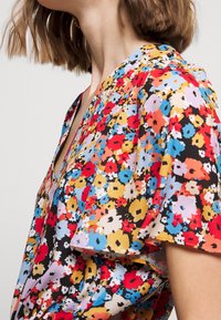 Floral blouse with a black background, featuring vibrant red, blue, yellow, and pink flowers. Short sleeves and a V-neck design. Soft texture.