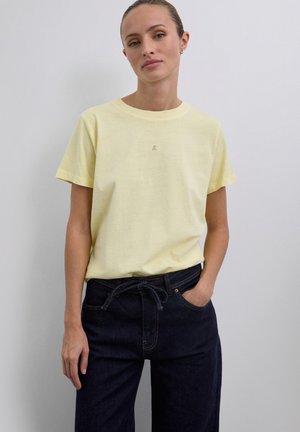 T-shirt en coton jaune à manches courtes et col rond, avec un petit logo au centre. Assorti à un pantalon large en denim foncé.