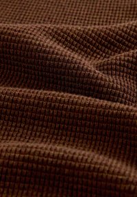 Tela de punto tipo gofre marrón con una textura suave, mostrada en primer plano con pliegues y sombras naturales que realzan el patrón.