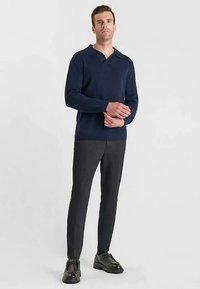 Marineblauer Strickpullover mit Polokragen, kombiniert mit dunkelgrauen Slim-Fit-Hosen. Dazu schwarze Leder-Schnürschuhe. Neutraler Hintergrund.