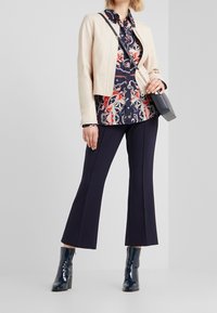 Béžová kožená bunda, květinová námořnická blůza, námořnické zvonové kalhoty a lesklé námořnické kotníkové boty; kabelka přes rameno s řetízkem.