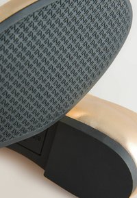 Obermaterial aus goldenem Leder mit einer strukturierten grauen Gummisohle und einem schwarzen Akzent-Absatz. Auffälliges Muster auf der Sohle für verbesserten Grip.