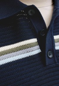 Polo en tricot bleu foncé avec des boutons noirs et des rayures horizontales en blanc, vert olive et bleu clair sur la poitrine.