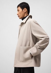 Beige lichtgewicht jacket met een relaxte pasvorm, met een kraag, een voorzak en subtiele stikdetails op de mouw.