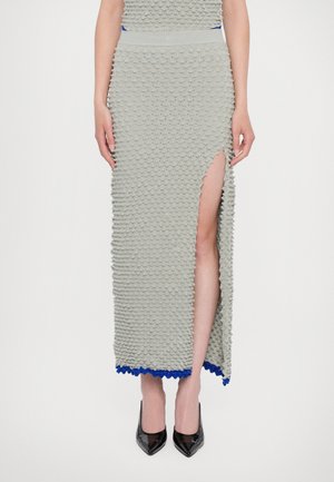 Knit maxi dress in light gray with textured, raised patterns, thigh-high slit, and scalloped hem in blue. Paired with black heels.
