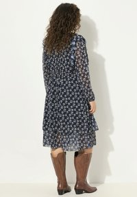 Vestido floral azul marino con superposición transparente, mangas con volantes y diseño en capas. Combinado con botas de vaquero marrones.
