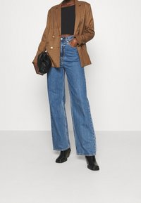 Brun rutigt blazer, skräddarsydd passform, dubbelknäppt med gyllene knappar. I kombination med vida blå denimjeans och svarta ankelboots.