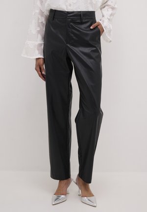 Pantalones de piel sintética negros con corte recto, bolsillos delanteros y un acabado brillante, combinados con tacones plateados de punta afilada.