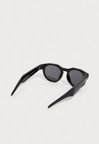 Mustat aurinkolasit, joissa on oktaalimuotoinen kehys, kapeat varret ja tummat linssit. Valmistettu kiiltävästä muovista, jossa on hienovarainen brändäys sivussa.