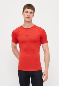 Tricou sportiv roșu dintr-un material neted și elastic. Are un decolteu rotund, mâneci scurte și un mic logo Nike negru pe piept.