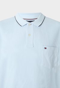 Gaiši zils polo krekls no teksturēta auduma, ar kontrastējošu apkakli ar melnu apdari, divām pogām un krūšu kabatu ar logotipu.
