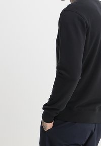 Felpa nera con maniche lunghe, polsini e orlo a coste. Texture morbida, design minimalista e vestibilità rilassata.