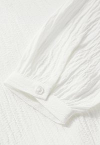 Witte textuurshirt met gathered lange mouwen, een knoopmanchet en lichte kreukels door de stof.