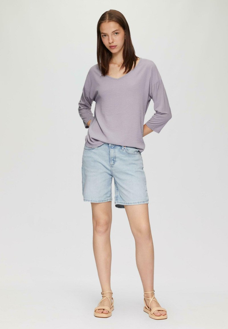 Hellblaues, strukturiertes Langarmshirt kombiniert mit hellen Jeansshorts und beigen Riemchensandalen, die ein lässiges Outfit ergeben.