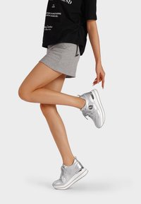 Sneaker atletici argento con rifinitura lucida e testurizzata, punta rotonda, allacciatura frontale, colletto imbottito e suola leggera, abbinati a una gonna grigia.